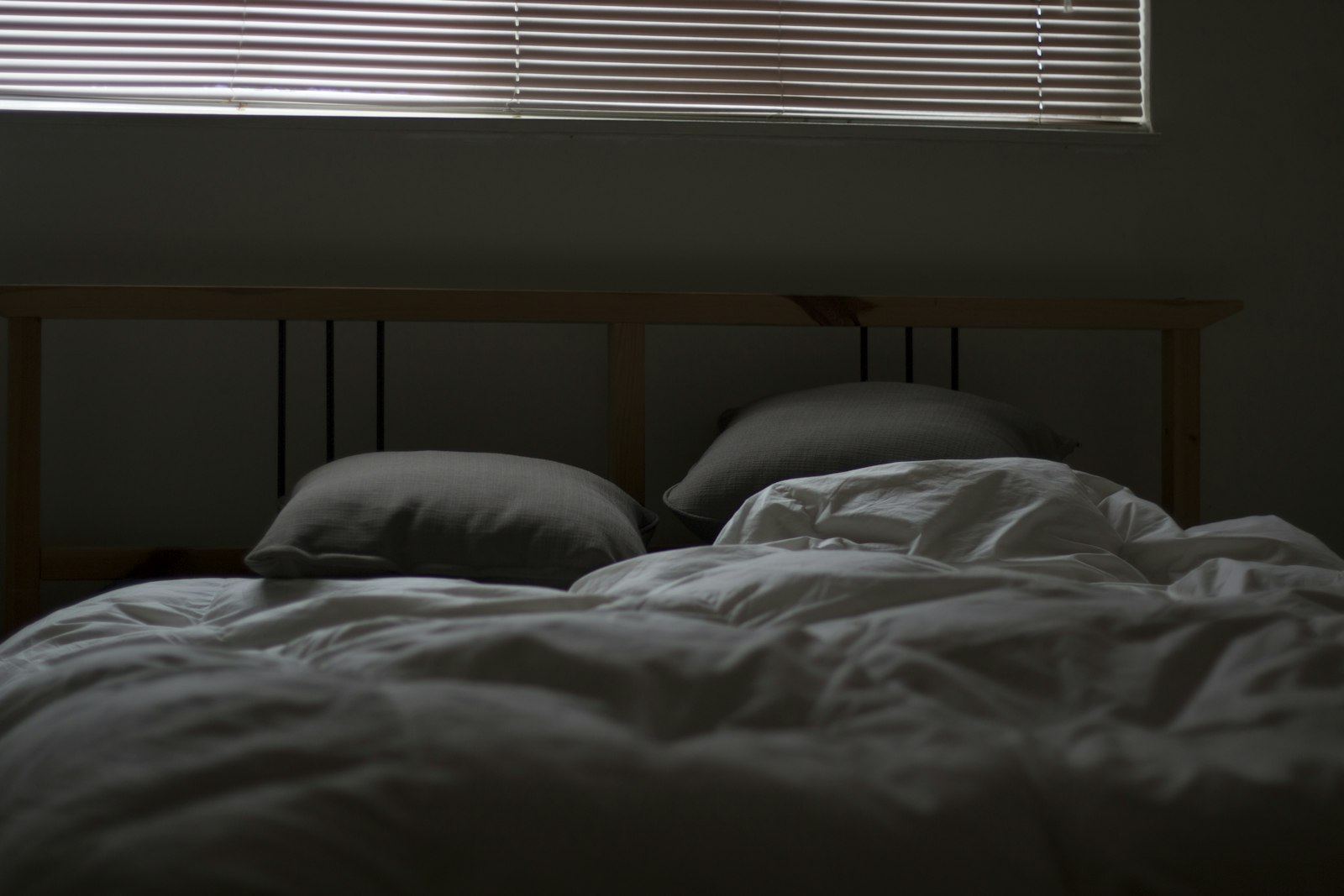 An unmade bed with light coming through the blinds