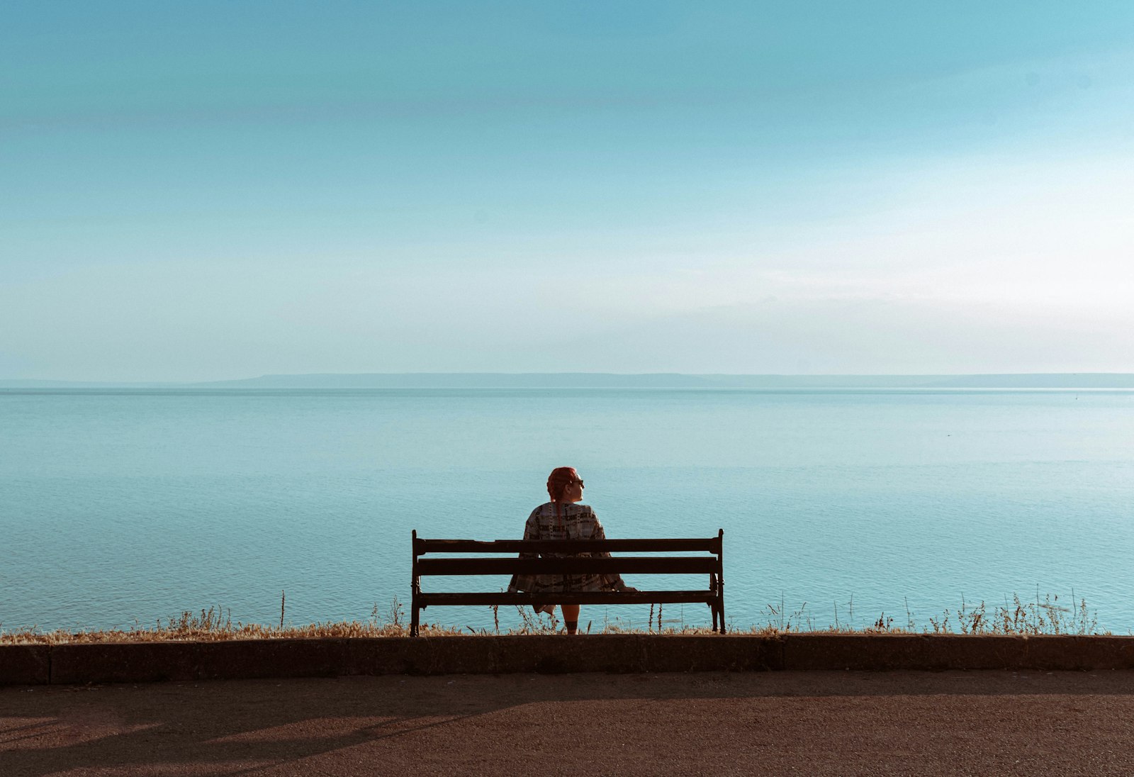 The back of a person sitting alone on a bench looking out at the sea