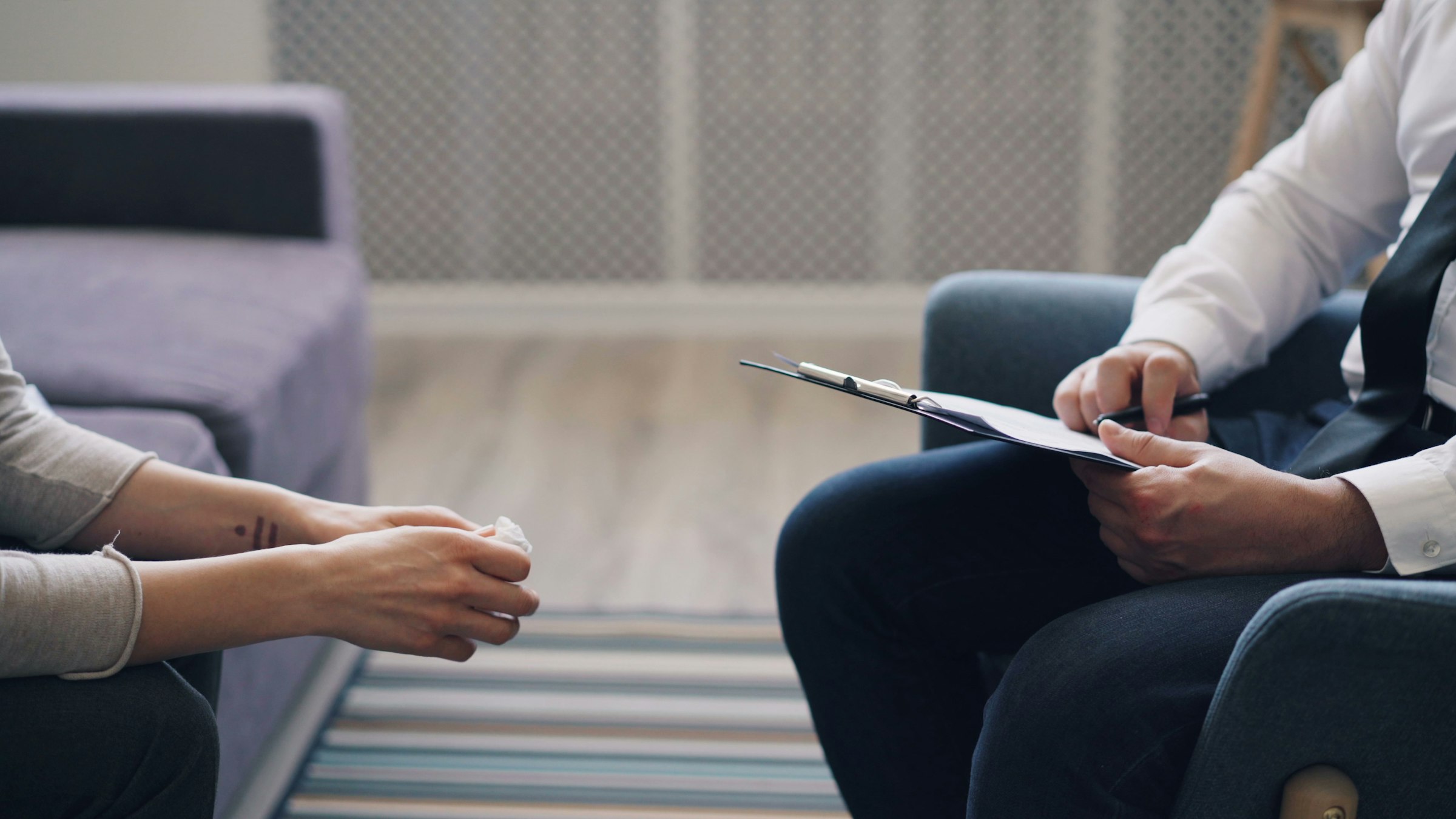 Hands taking notes on a clipboard during a consultation, facing another person's hands