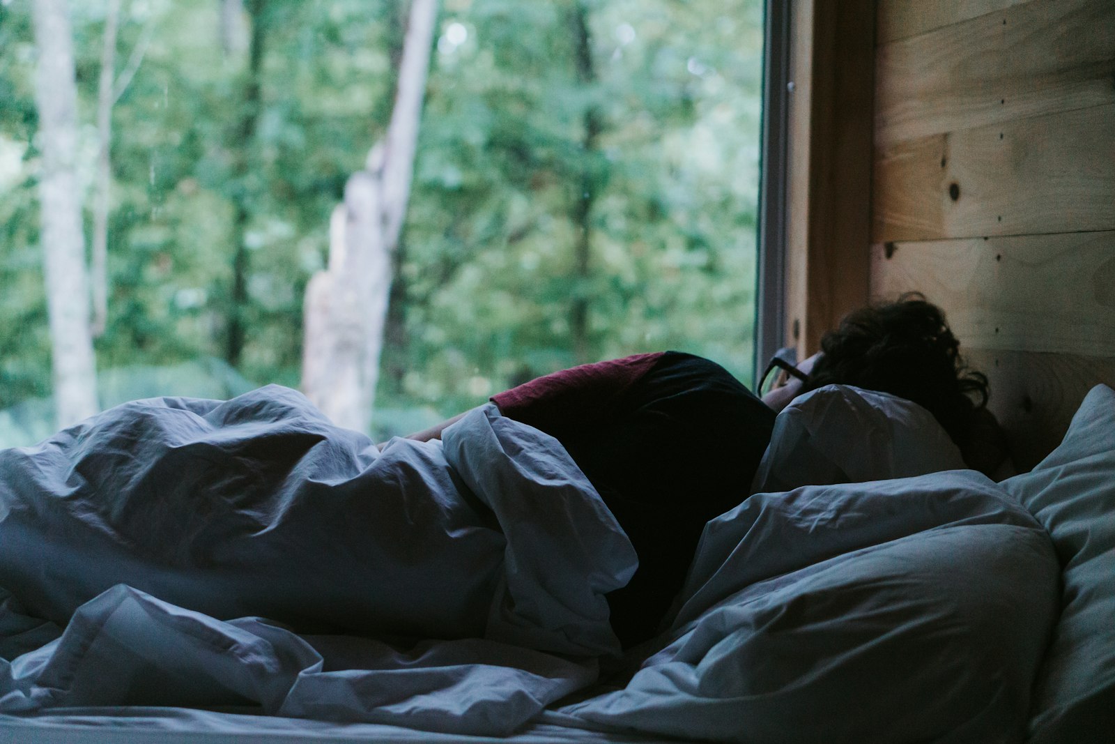 A person lying in bed under a blanket, seen from behind
