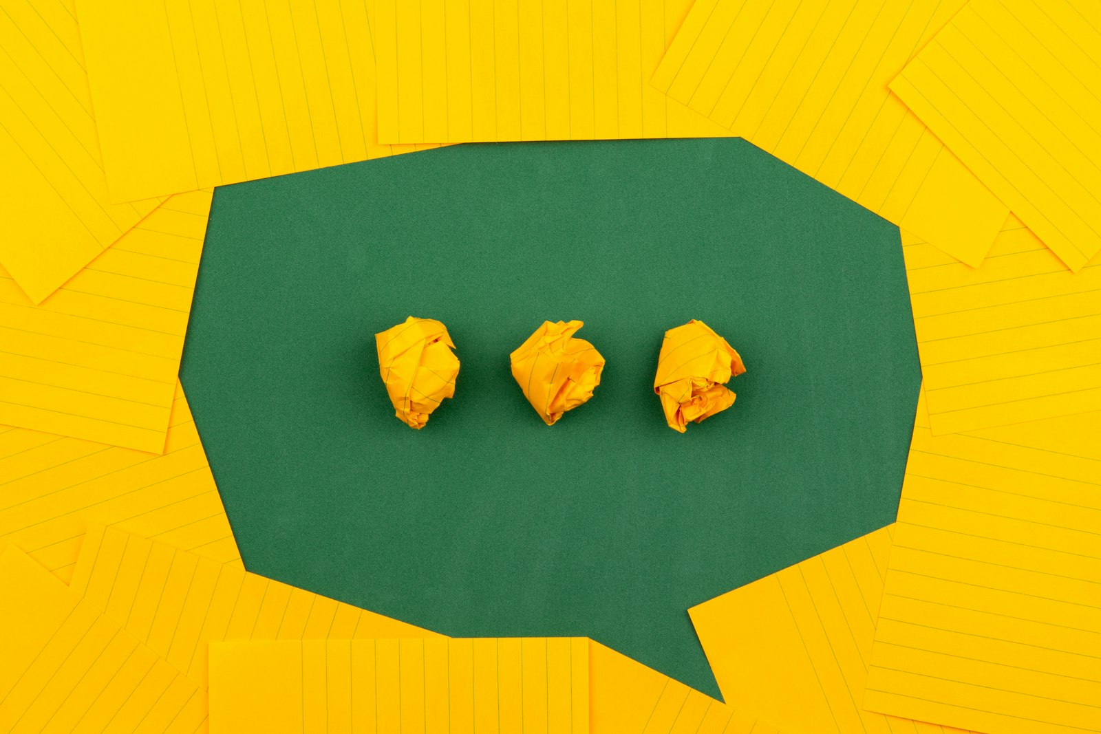 Crumpled scraps of yellow paper inside a speech-bubble shape cut from paper