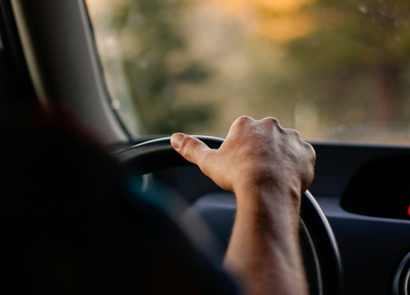 A hand on a steering wheel in daylight