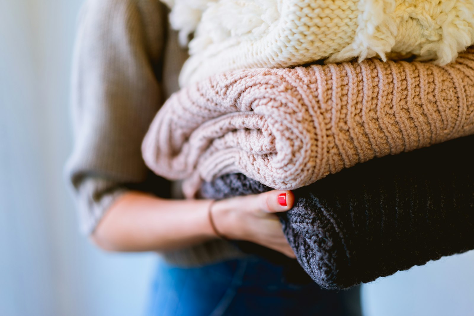 Hands holding a stack of folded knit sweaters