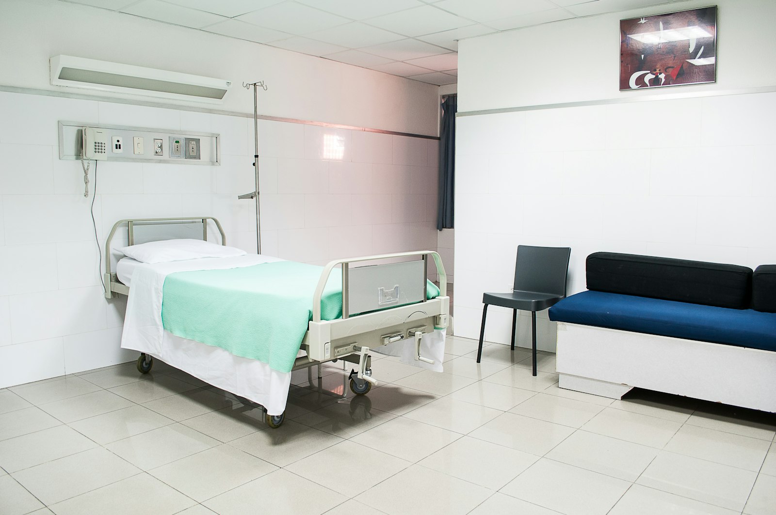 A hospital-style bed beside a small couch in a bare room