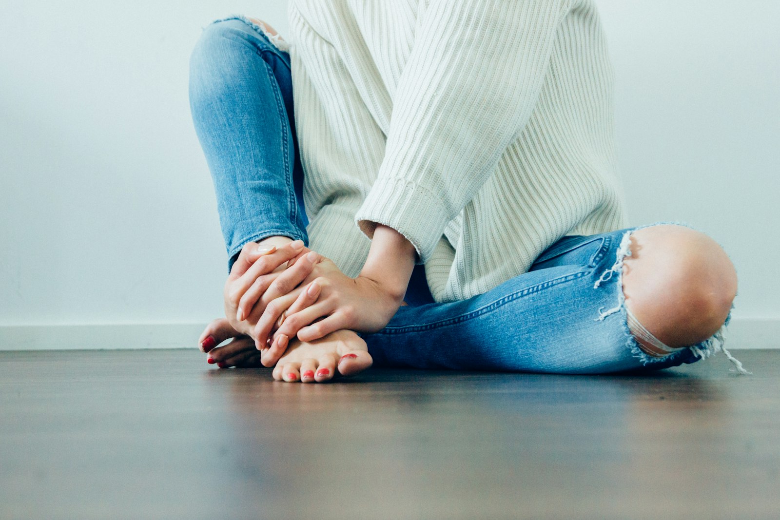 A person sitting on the floor holding their bare feet in both hands