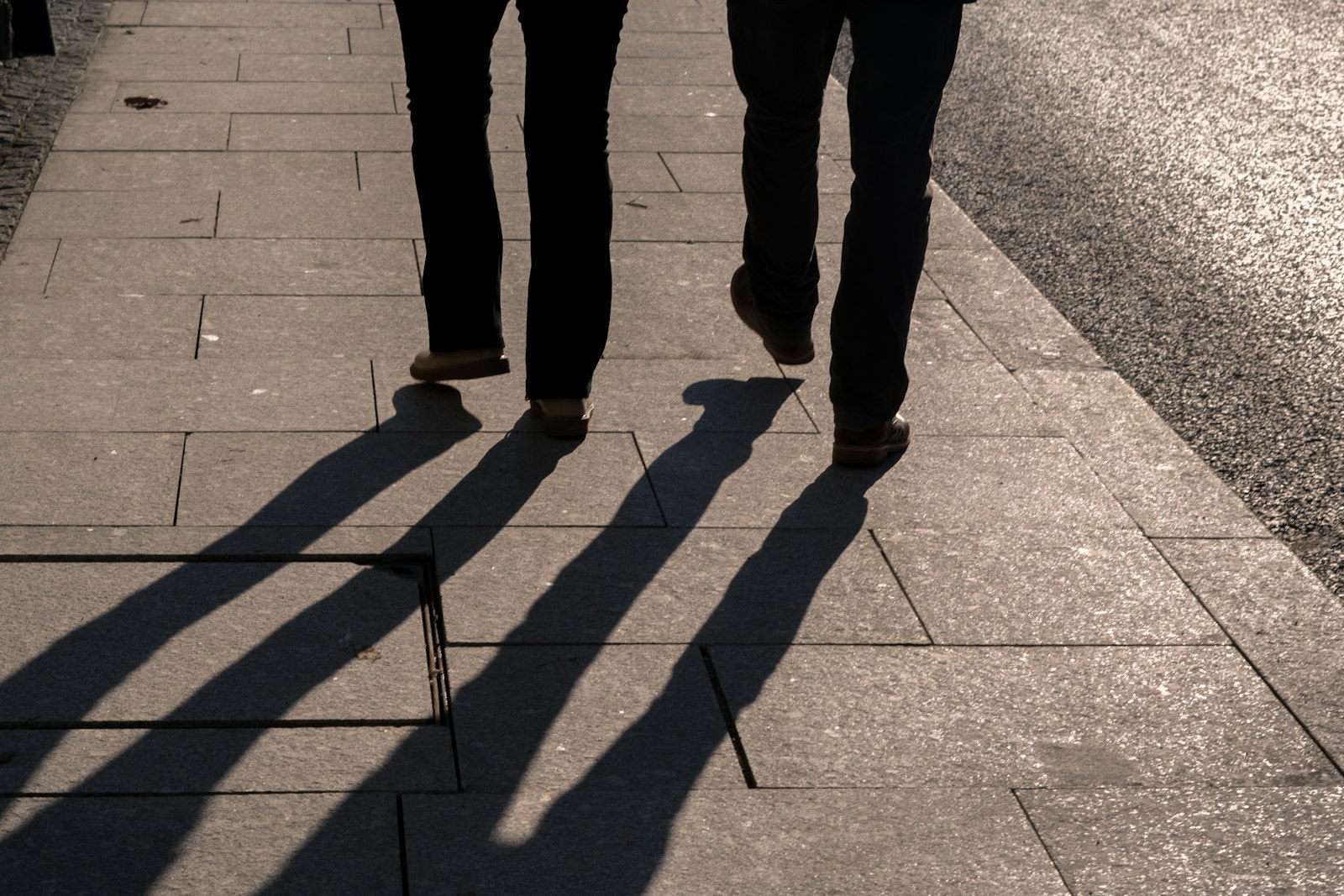 The long shadows of two people walking on a pavement